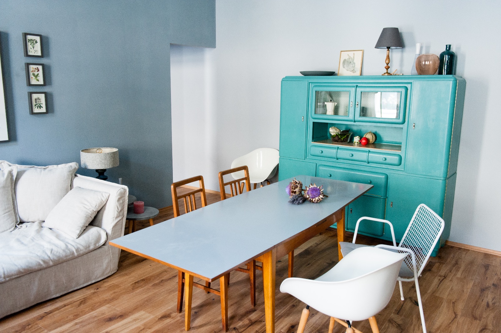 Espace de vie avec une armoire vintage turquoise, une table à manger gris clair sur des pieds en chêne et un canapé, à côté deux chambres pour une famille à Vienne pour un temps