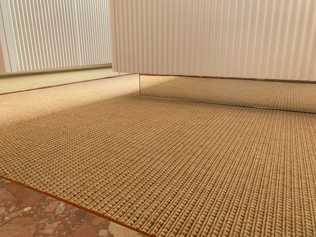 Floor transition of red marble between herringbone parquet and sand coloured sisal rug with a red brown border
