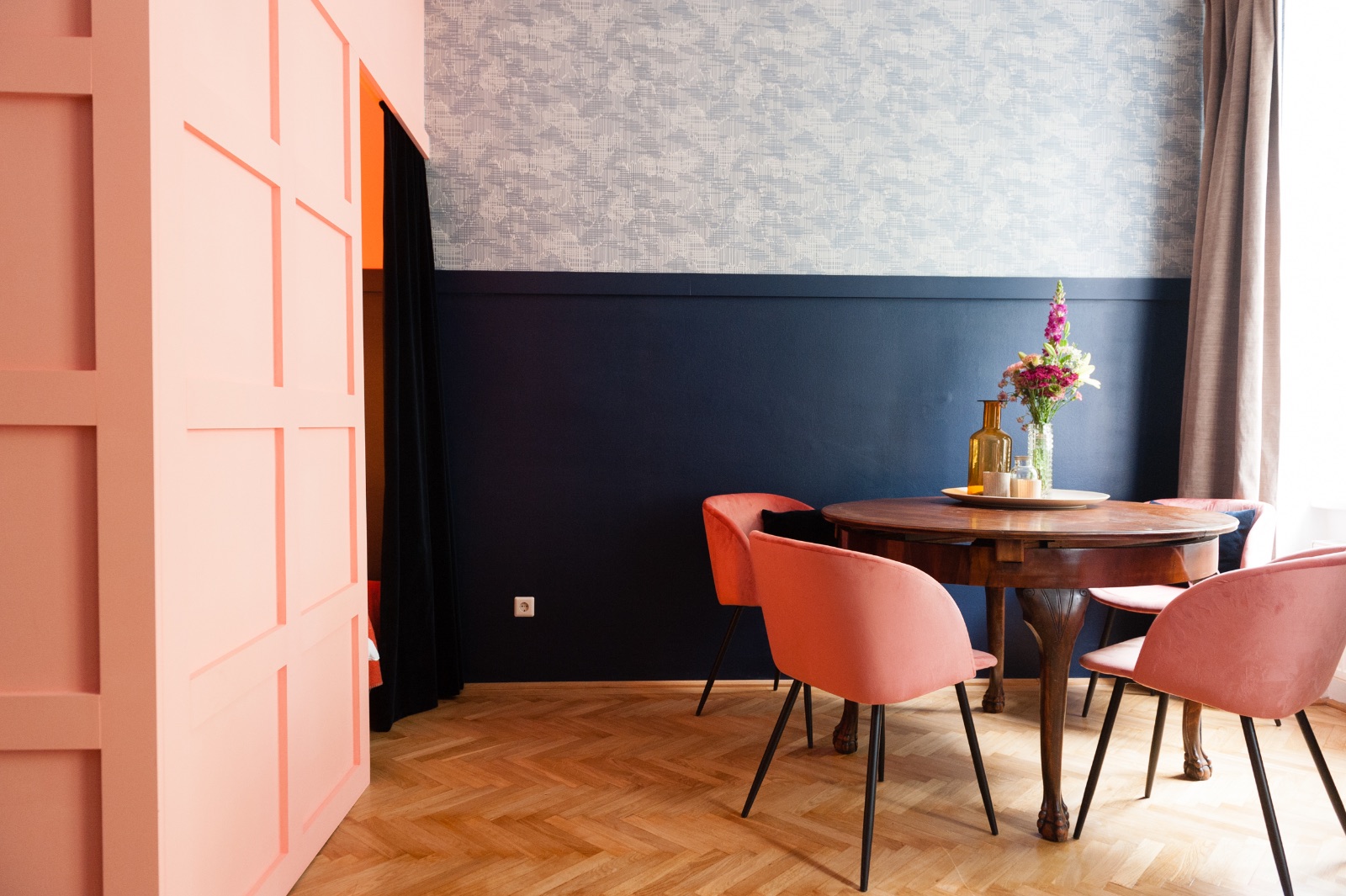 Living space of a furnished apartment in Vienna with an old leather trunk as a coffee table, a two tone blue wall, a carved wooden cabinet and herringbone parquet