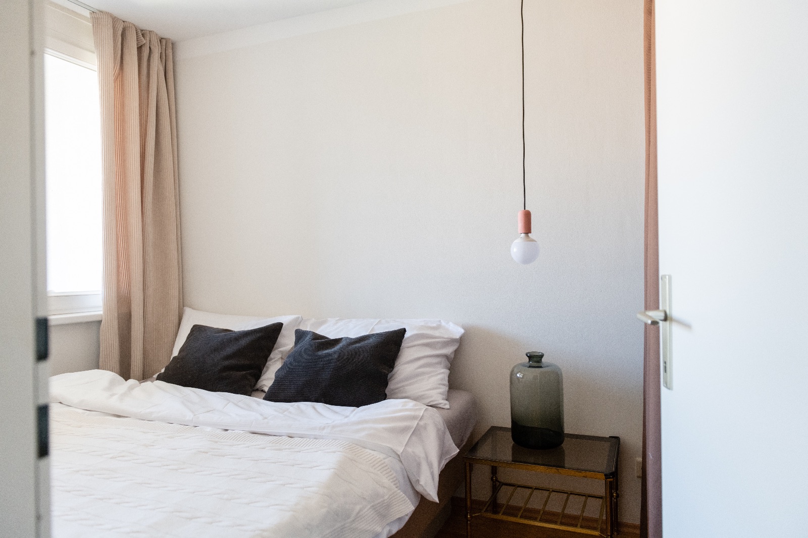 Furnished apartment in Vienna, bedroom with linen bed and pendant lamp, hallway with birch wallpaper and mirror, living room with grey velvet sofa by the window