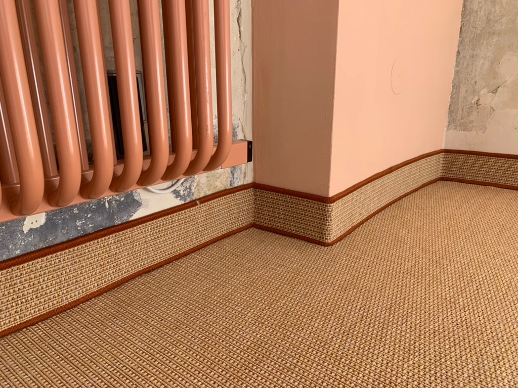 Transition de sol en marbre rouge entre parquet en chevron et tapis en sisal couleur sable a bordure brun rouge