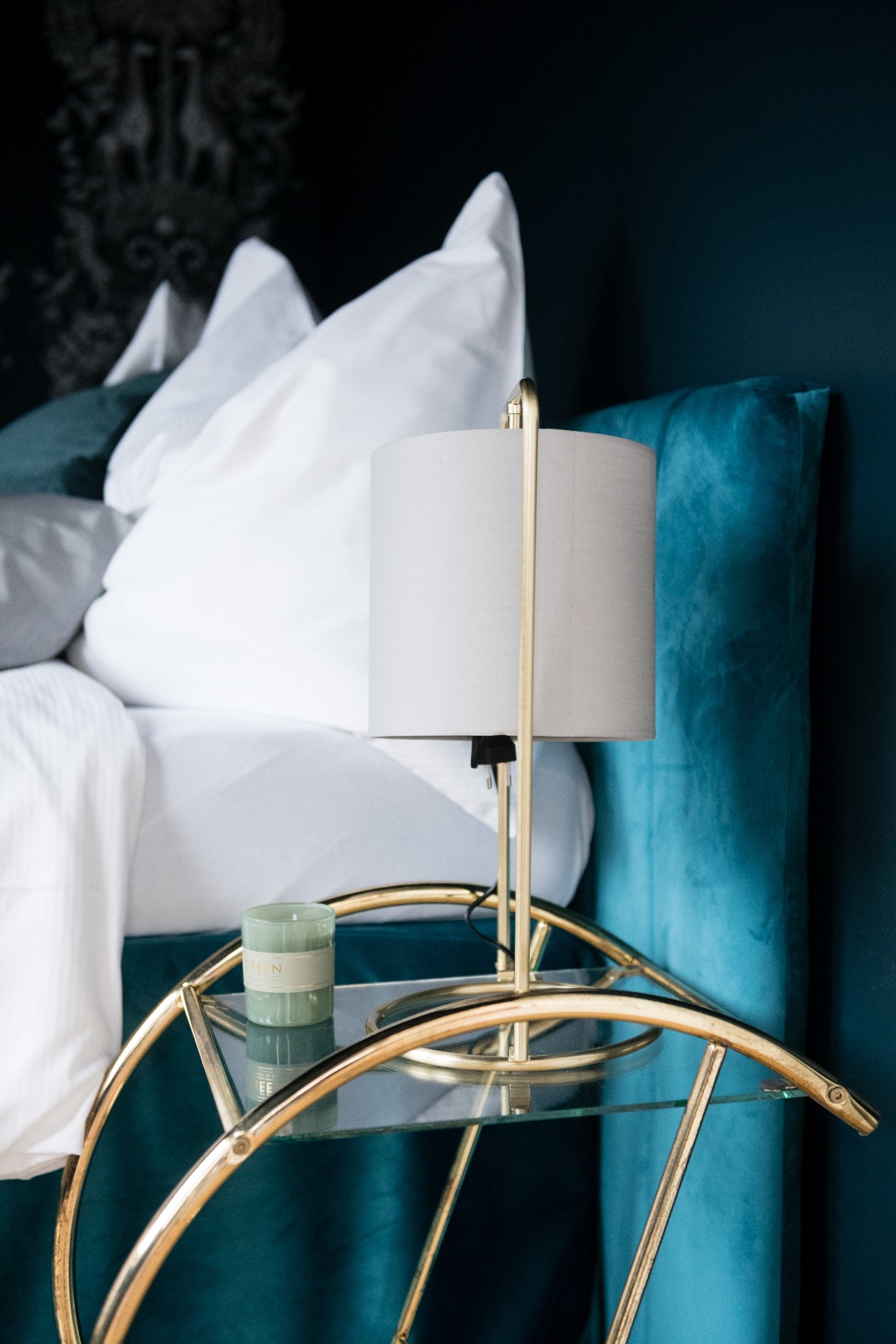 Schlafzimmer in tiefem Petrol mit Samtkopfteil, weißem Bettzeug, dunkler Tiermuster-Tapete und Messing-Beistelltisch mit Lampe